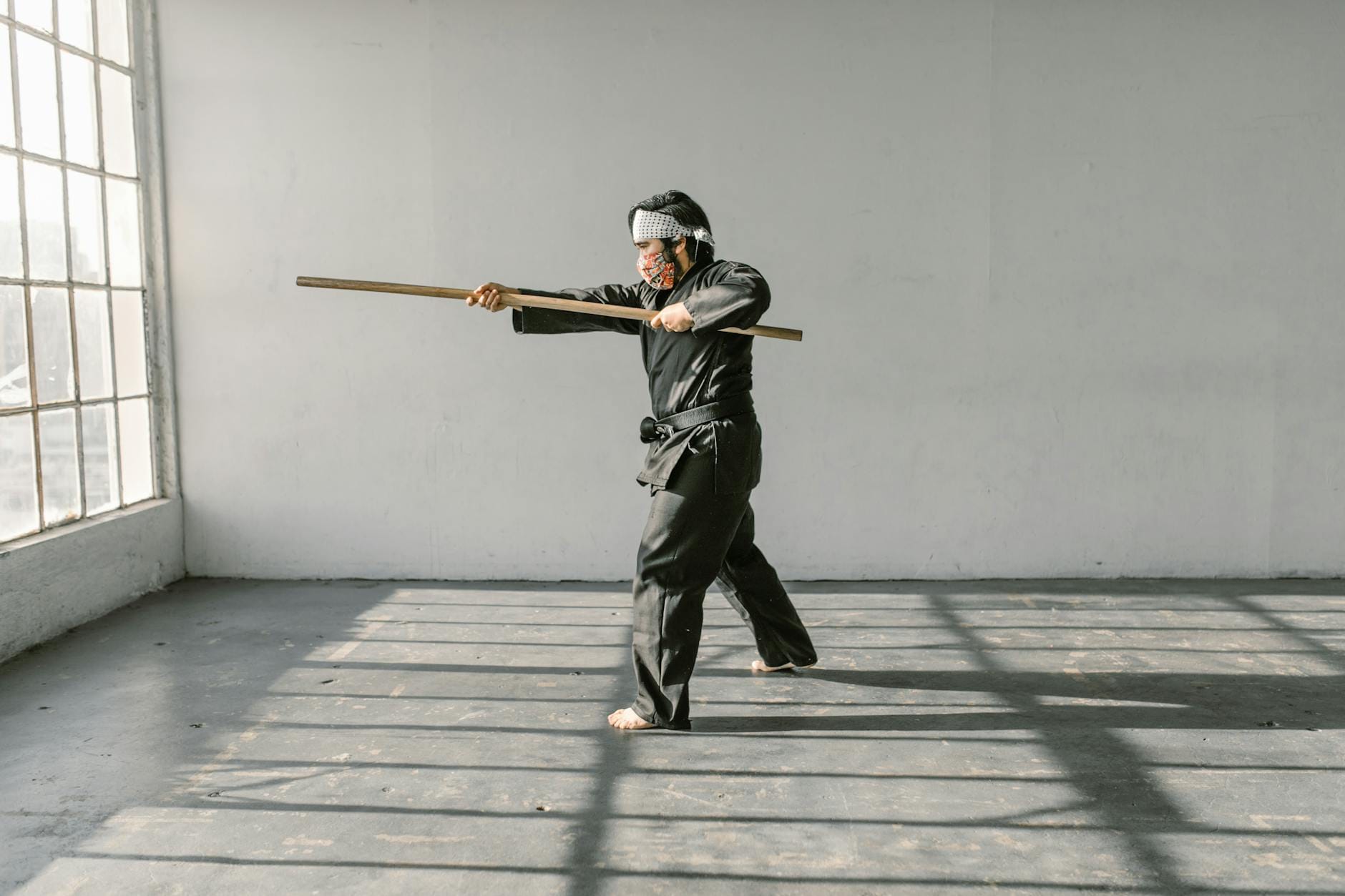 Adept w czarnym gi trenuje z drewnym kijem w jasnej sali treningowej