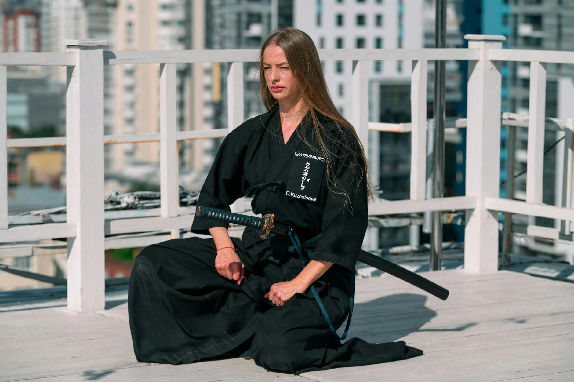 Kobieta w czarnym kimonie medytuje z mieczem na dachu miasta