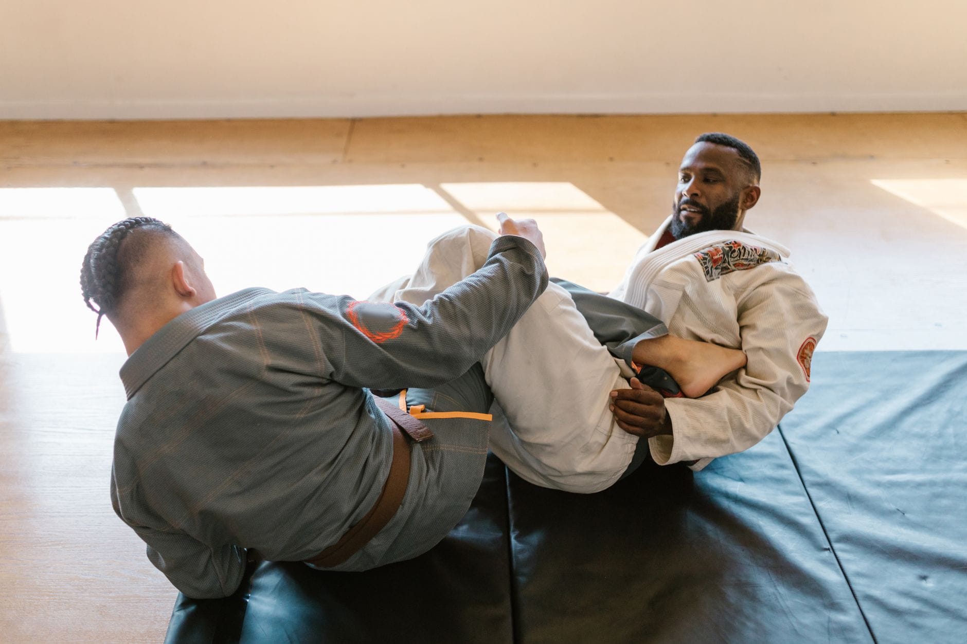 Dwóch mężczyzn trenuje jujutsu w kimonach na macie w sali